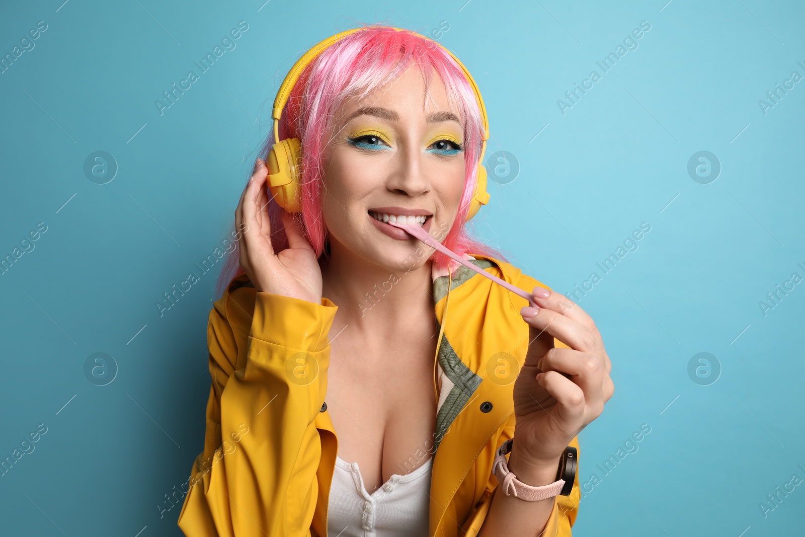 Photo of Fashionable young woman in pink wig with headphones chewing bubblegum on yellow background