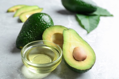 Photo of Bowl of natural oil and avocados on grey stone background