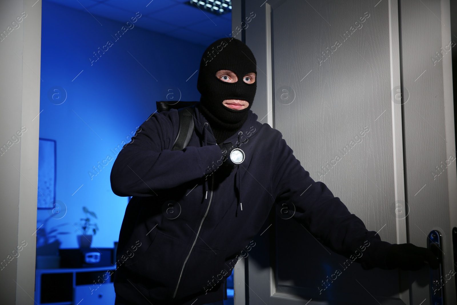 Photo of Thief with flashlight breaking into house at night