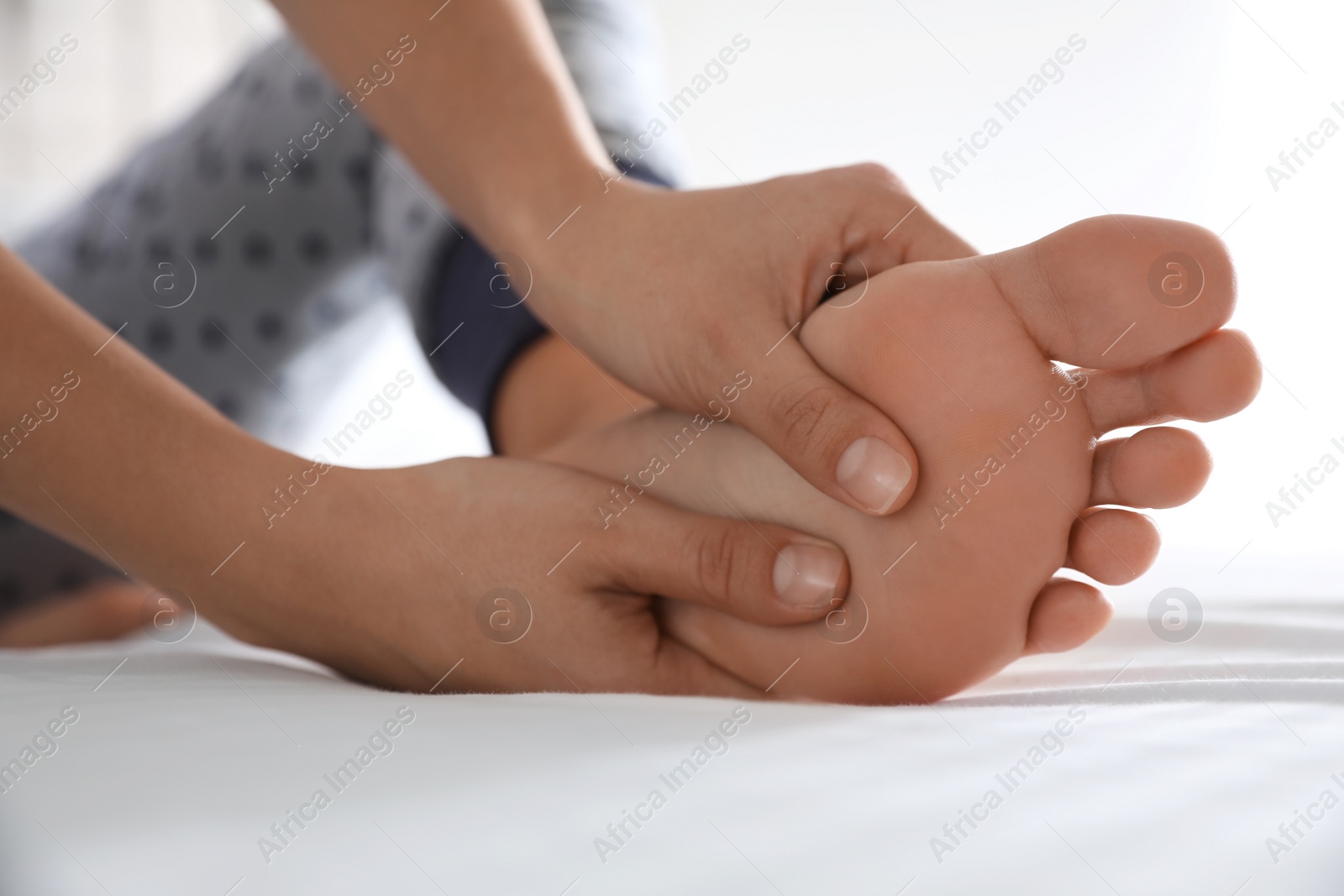 Photo of Young woman suffering from pain in foot on bed, closeup