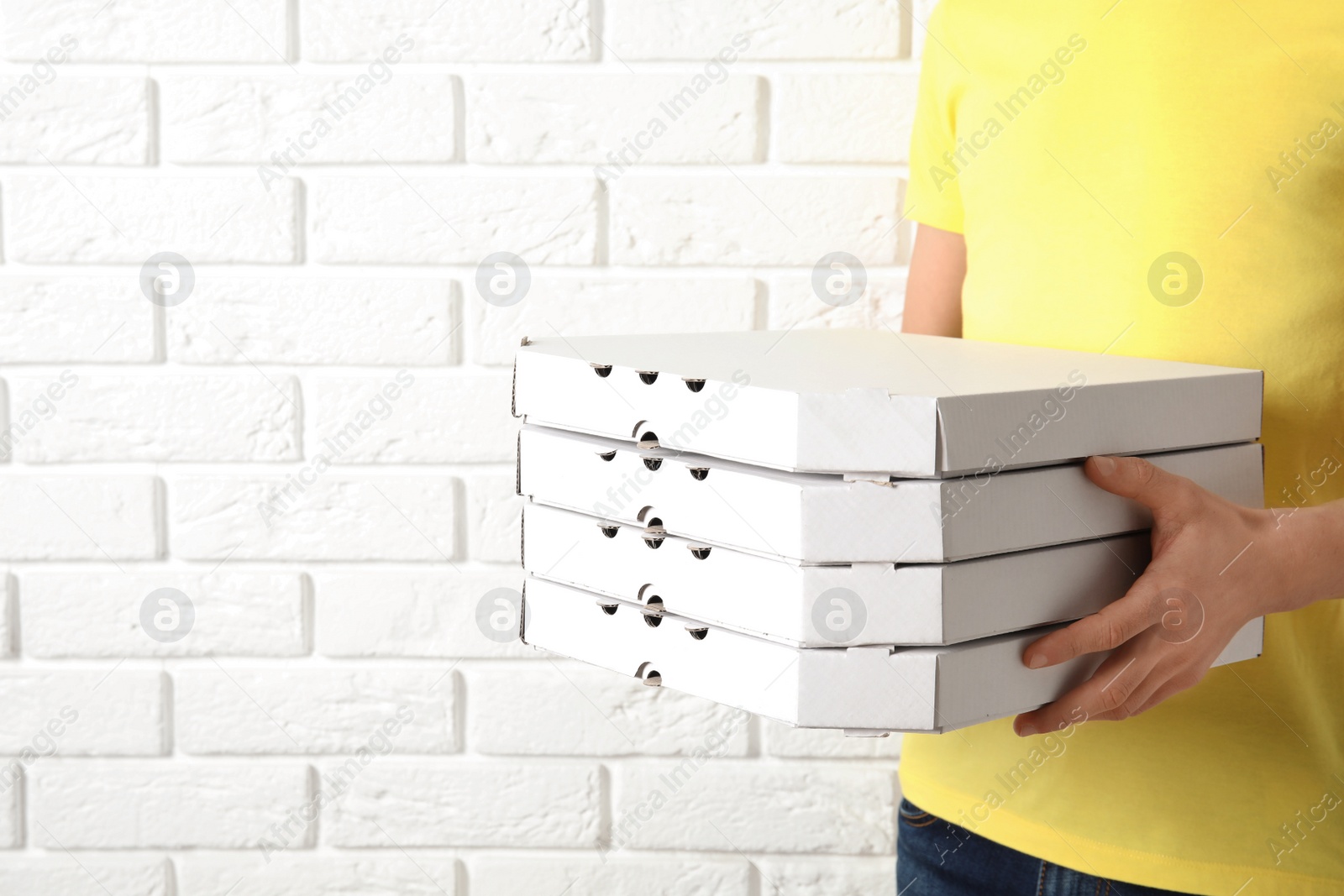 Photo of Courier holding pizza boxes near white brick wall, closeup with space for text. Food delivery service