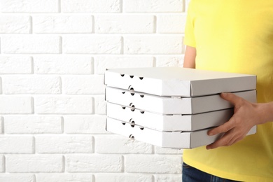 Courier holding pizza boxes near white brick wall, closeup with space for text. Food delivery service