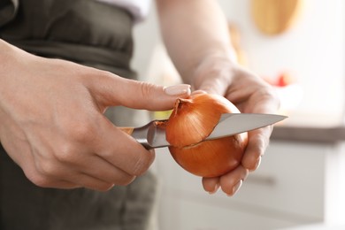 Photo of Woman peeling fresh onion with knife indoors, closeup