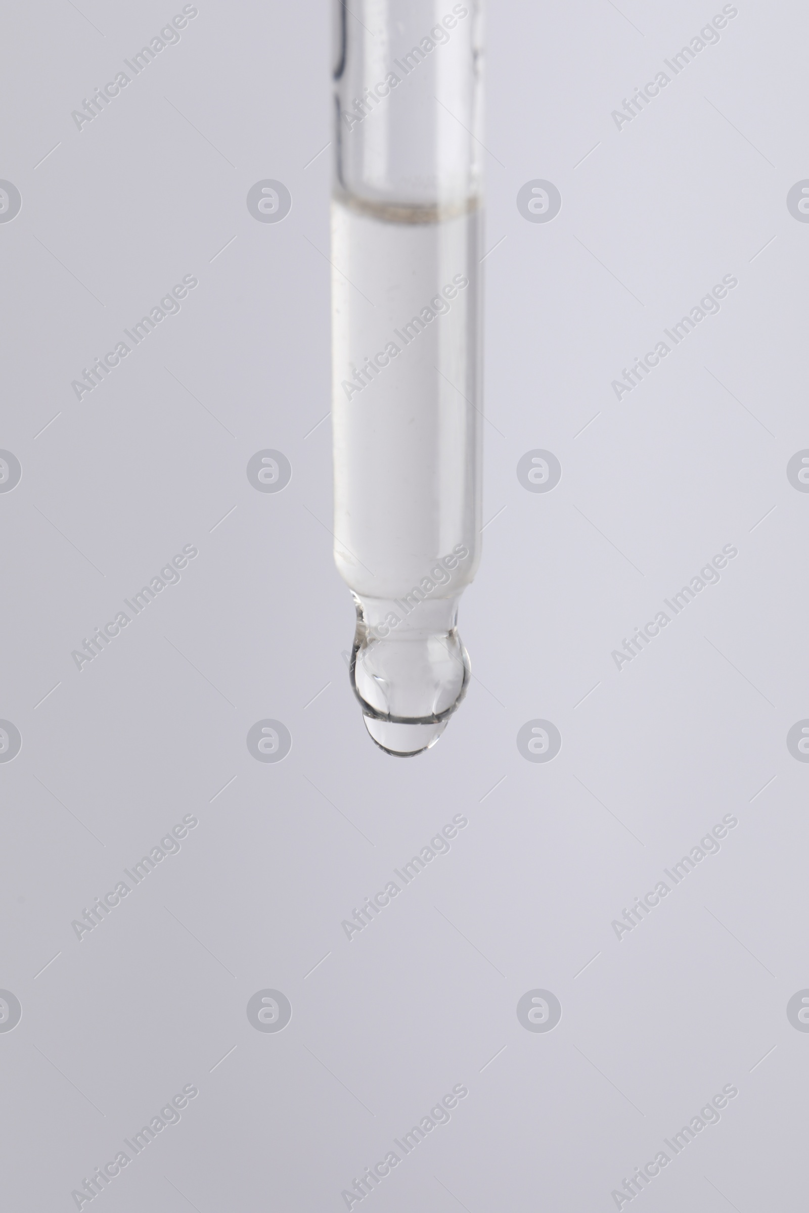 Photo of Dripping cosmetic serum from pipette on light grey background