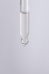 Dripping cosmetic serum from pipette on light grey background