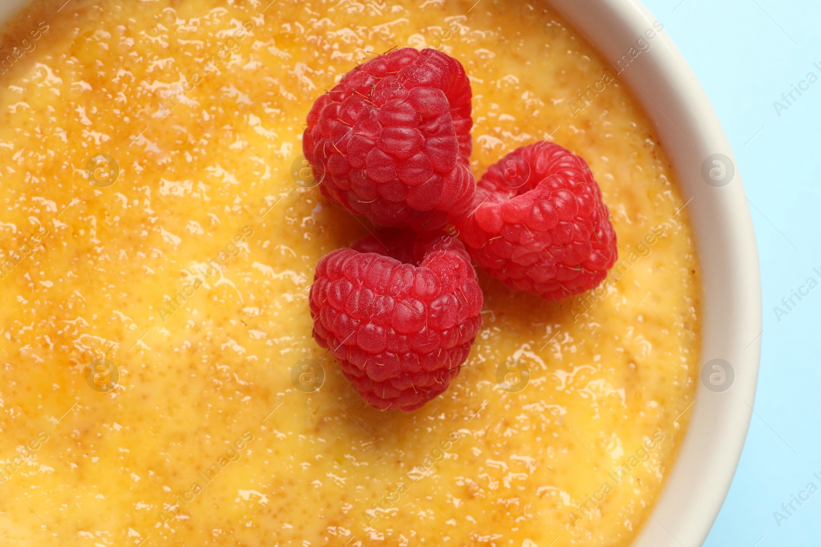 Photo of Delicious creme brulee with fresh raspberries on light blue background, top view