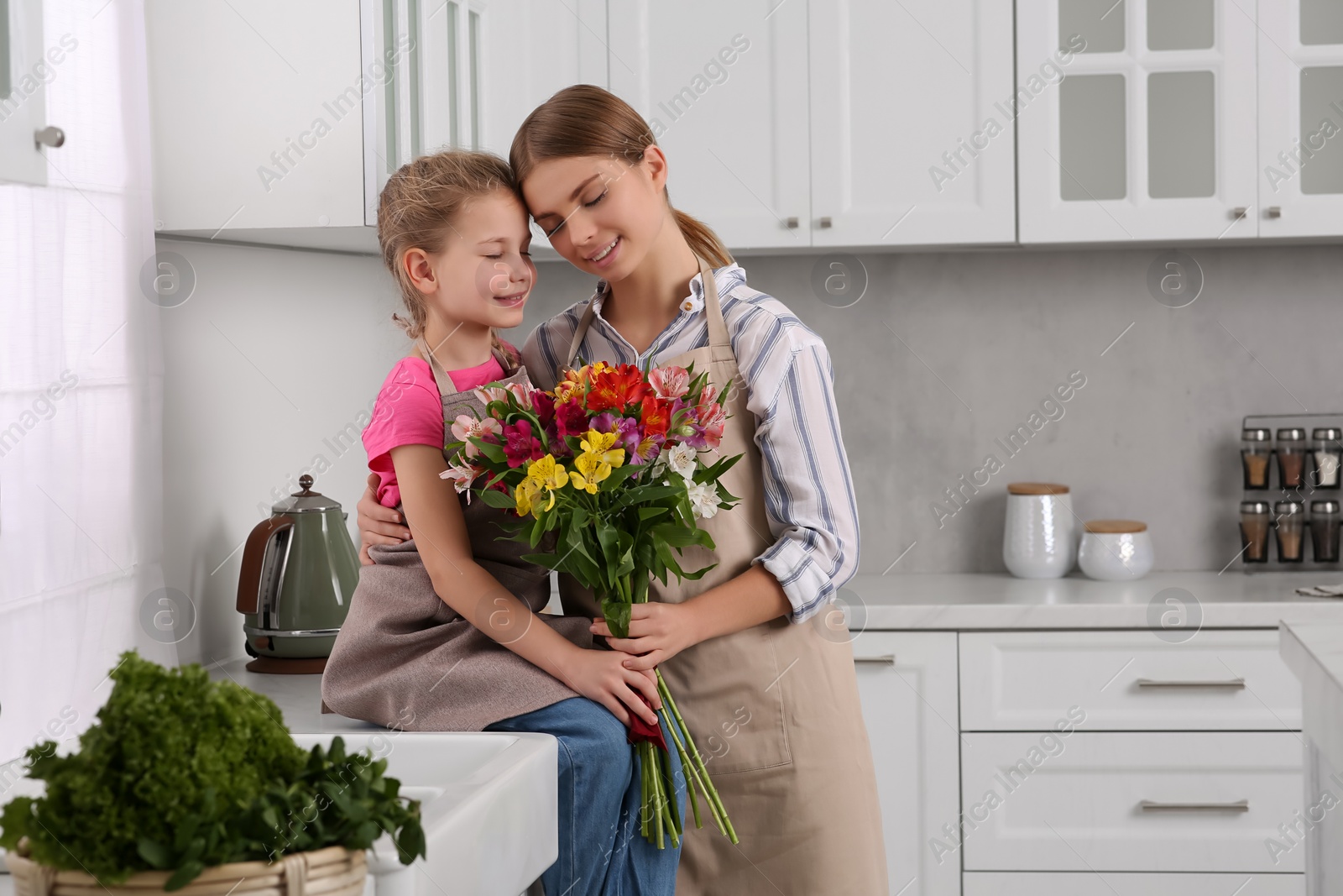 Photo of Little daughter congratulating mom with bouquet of flowers in kitchen. Happy Mother's Day