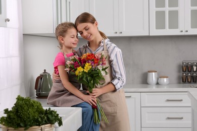 Photo of Little daughter congratulating mom with bouquet of flowers in kitchen. Happy Mother's Day