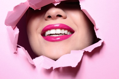 View of beautiful young woman with perfect lips makeup through hole in color paper