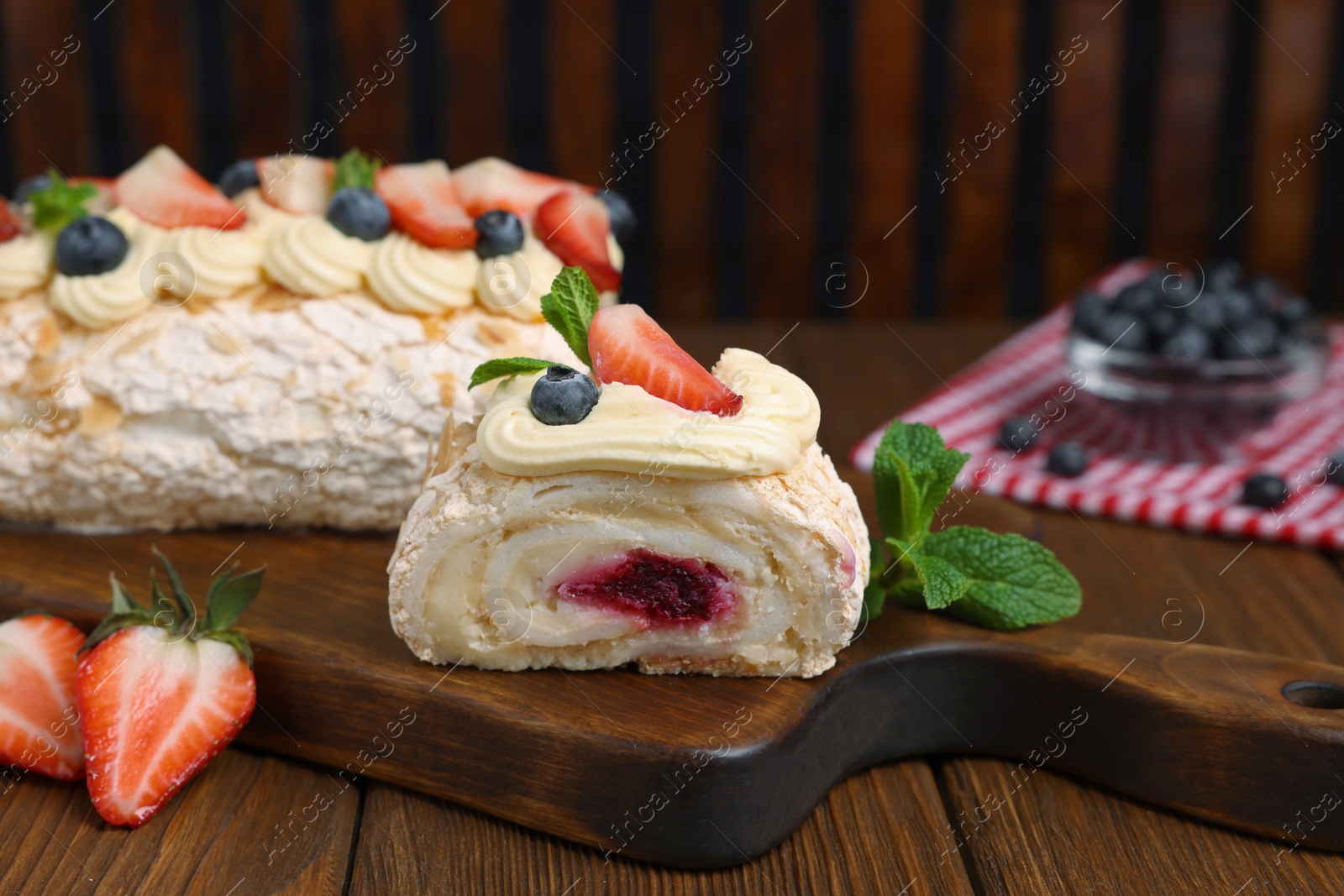 Photo of Tasty meringue roll with jam, cream, strawberry, blueberry and mint on wooden table, closeup