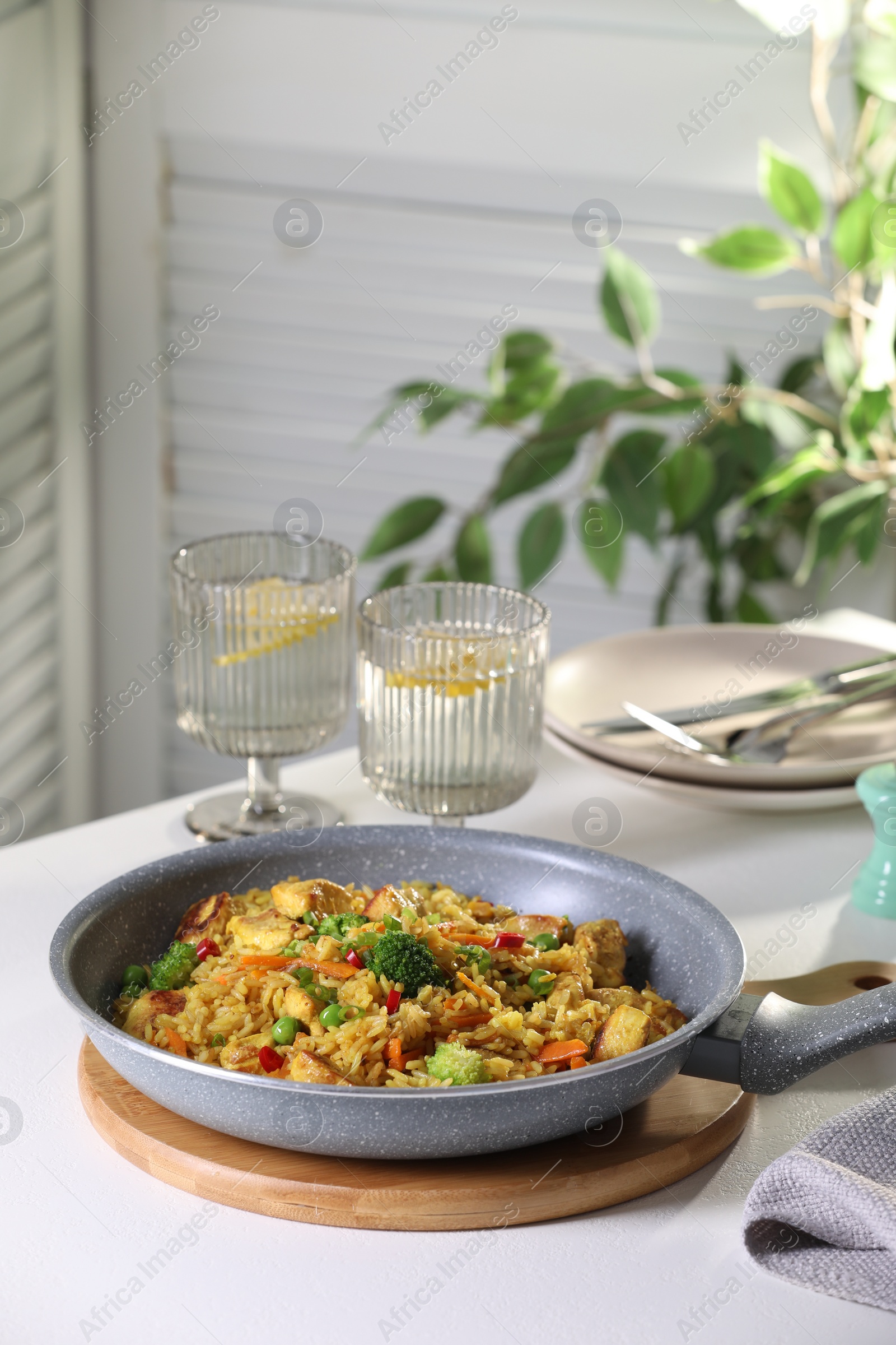 Photo of Tasty rice with meat and vegetables in frying pan on white table indoors