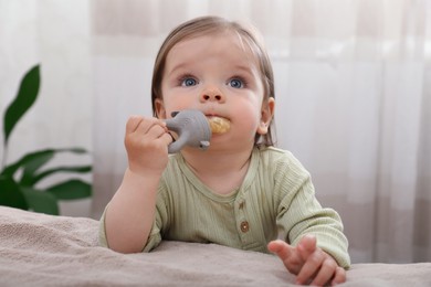 Photo of Cute baby girl with nibbler near bed at home