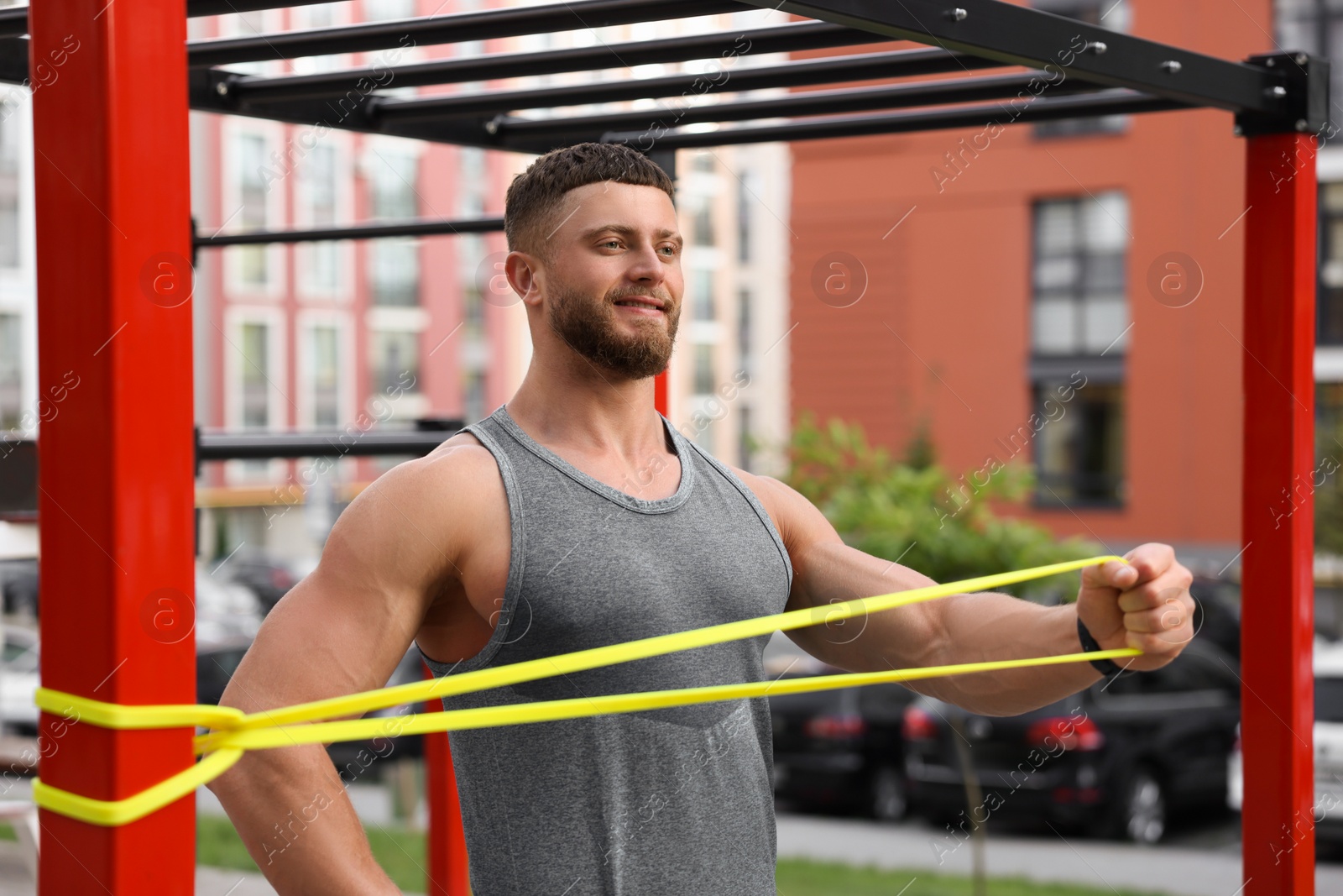 Photo of Muscular man doing exercise with elastic resistance band on sports ground