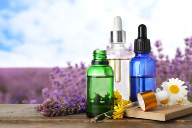 Image of Bottles of essential oils and wildflowers on wooden table against blurred background. Space for text