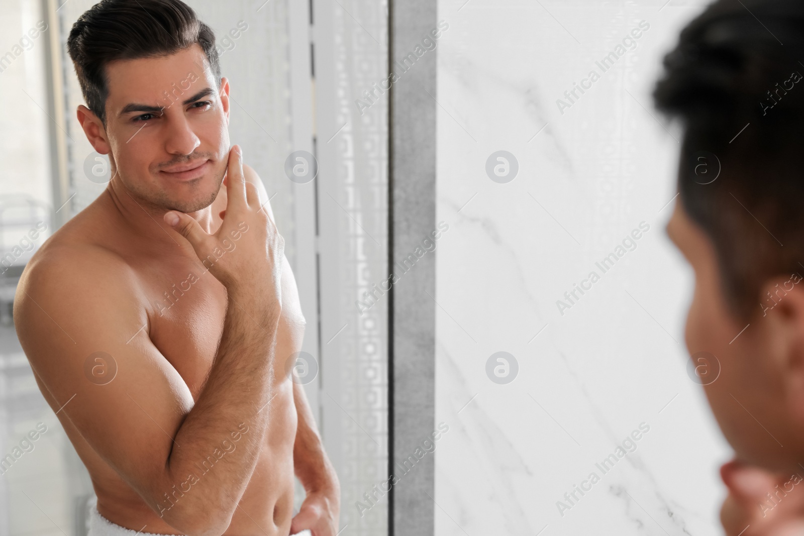 Photo of Handsome man touching his smooth face after shaving near mirror in bathroom