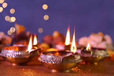 Diwali celebration. Diya lamps on shiny golden table against blurred lights, closeup