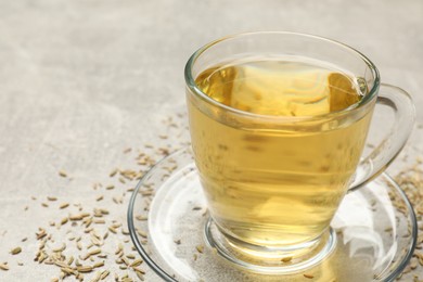 Photo of Aromatic fennel tea in cup and seeds on light grey table, closeup. Space for text
