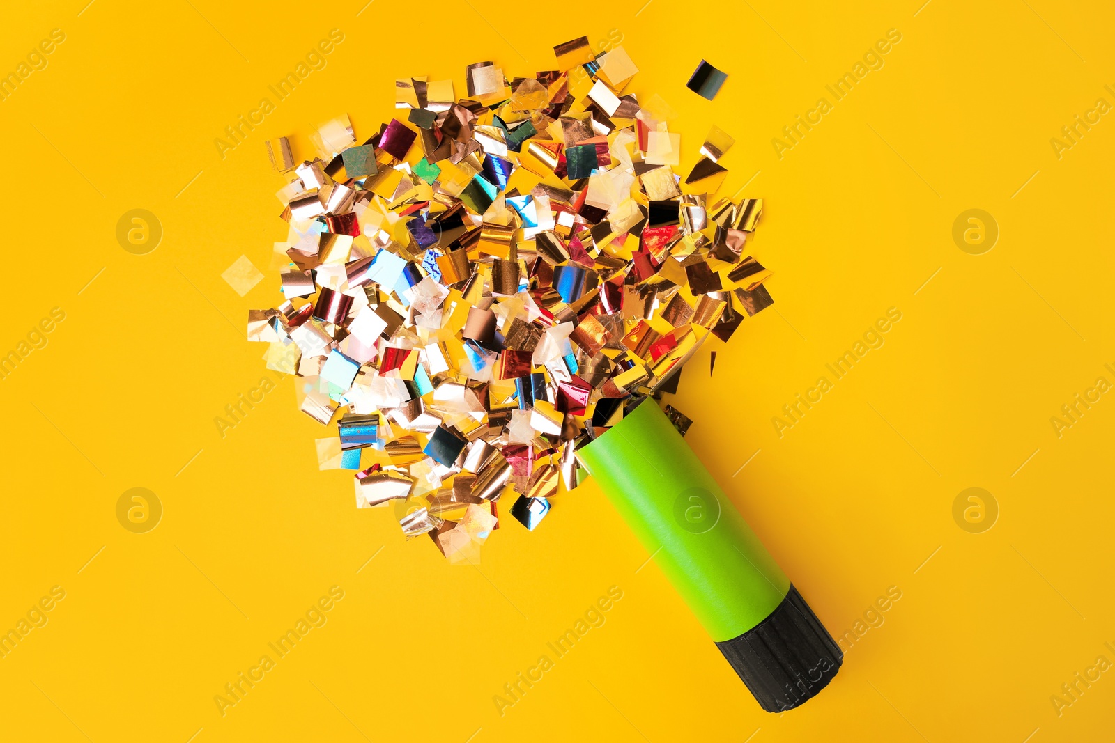 Photo of Shiny colorful confetti bursting out of party popper on yellow background, flat lay