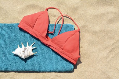 Photo of Towel, bra and seashell on sand, top view with space for text. Beach accessories