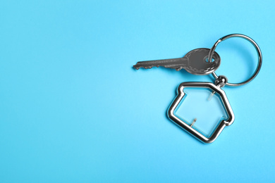 Photo of Key with trinket in shape of house on light blue background, top view and space for text. Real estate agent services
