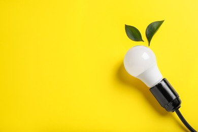 Photo of Light bulb and green leaves on yellow background, flat lay. Space for text