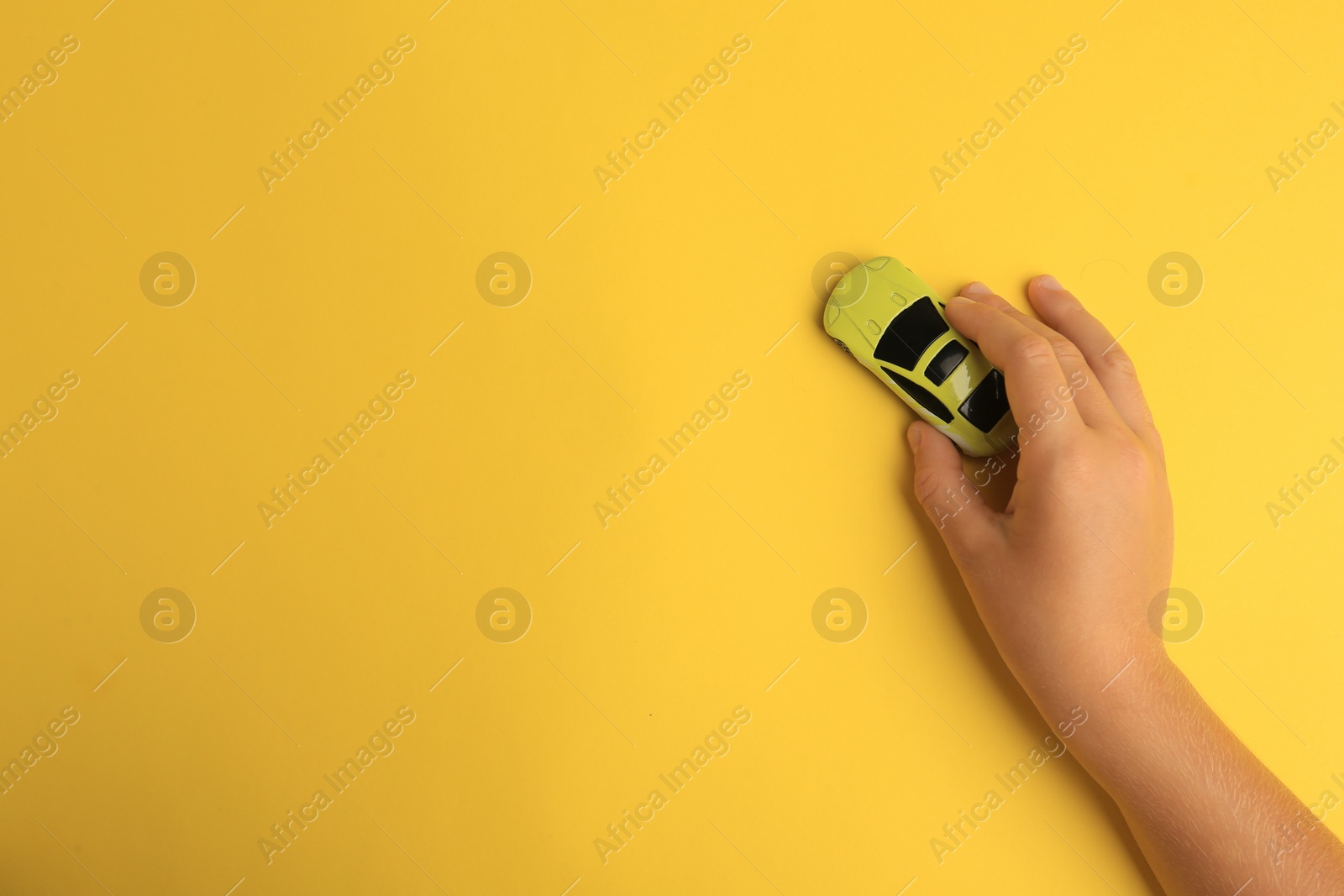 Photo of Child playing with toy car on yellow background, top view. Space for text