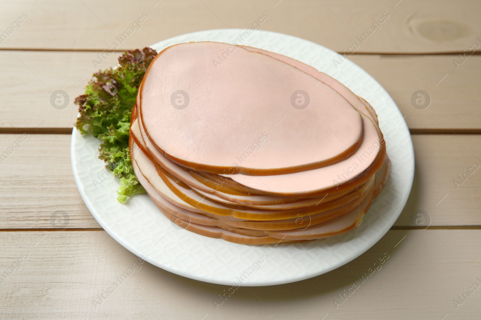 Photo of Slices of delicious boiled sausage with lettuce on beige wooden table