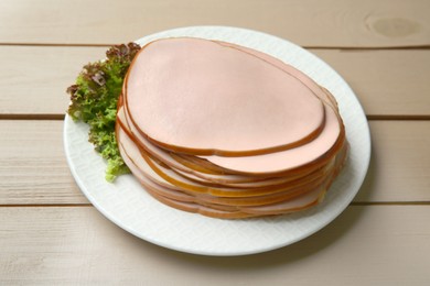 Photo of Slices of delicious boiled sausage with lettuce on beige wooden table