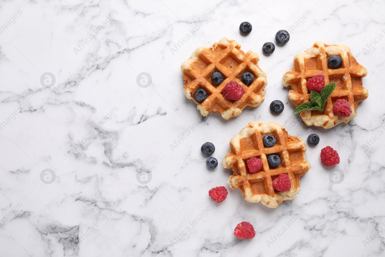 Photo of Delicious Belgian waffles with fresh berries and mint on white marble table, flat lay. Space for text