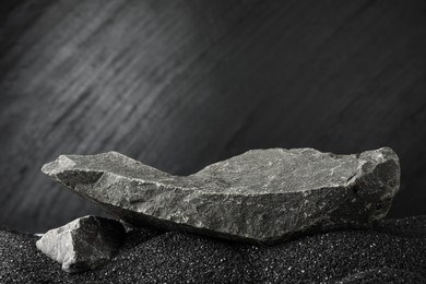 Photo of Presentation of product. Stone podium on black sand against dark textured background. Space for text