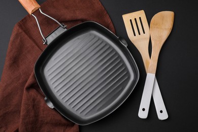 Wooden kitchen utensils and frying pan on black table, flat lay