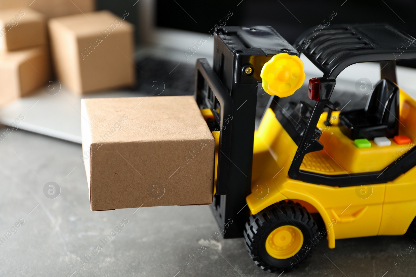 Photo of Toy forklift with box near laptop on table. Logistics and wholesale concept