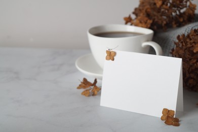 Dried hortensia flowers, blank card and cup of hot drink on white marble table, space for text