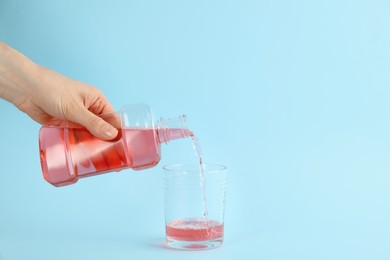 Photo of Woman pouring mouthwash into glass on light blue background, closeup. Space for text