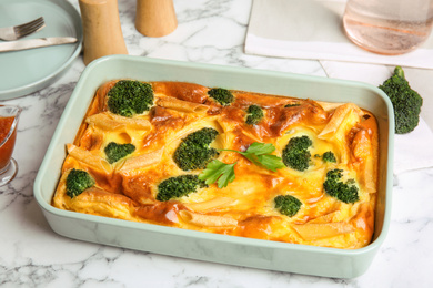 Photo of Tasty broccoli casserole in baking dish on white marble table