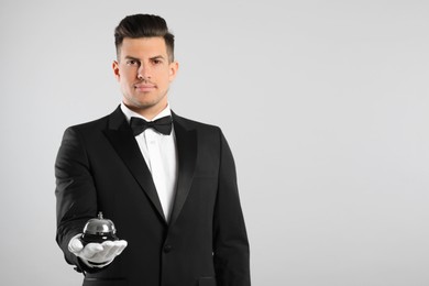 Handsome butler holding service bell on grey background, space for text