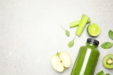 Green juice in bottle and fresh ingredients on light grey table, flat lay. Space for text