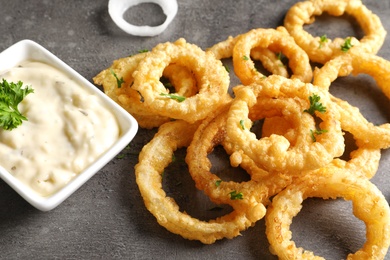 Homemade crunchy fried onion rings with sauce on color table, closeup