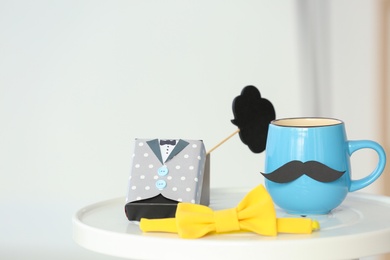 Cup with mustache, gift box and bow tie on table. Father's day celebration