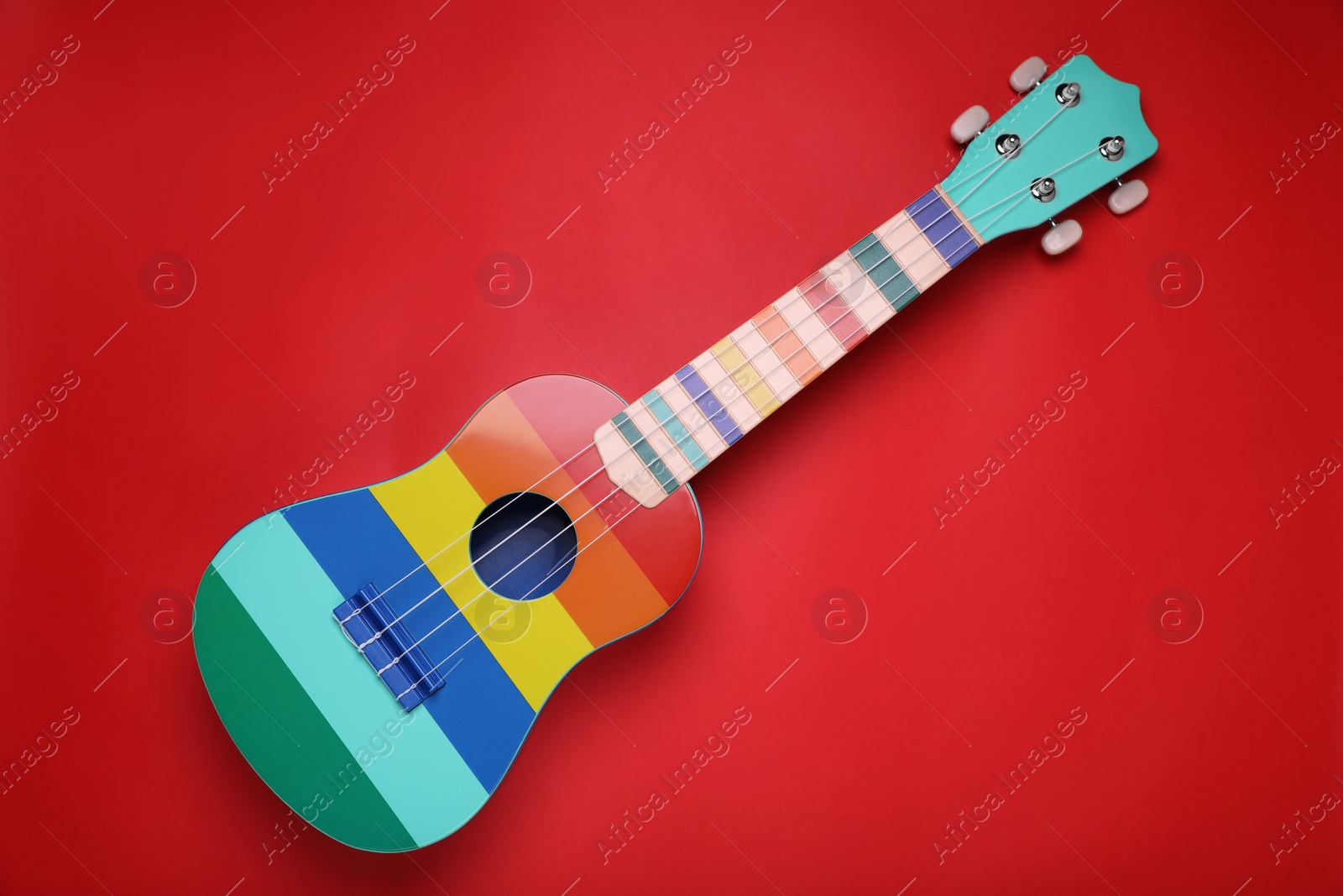 Photo of Colorful ukulele on red background, top view. String musical instrument