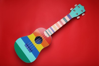 Colorful ukulele on red background, top view. String musical instrument