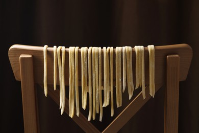 Photo of Homemade pasta drying on chair against dark background