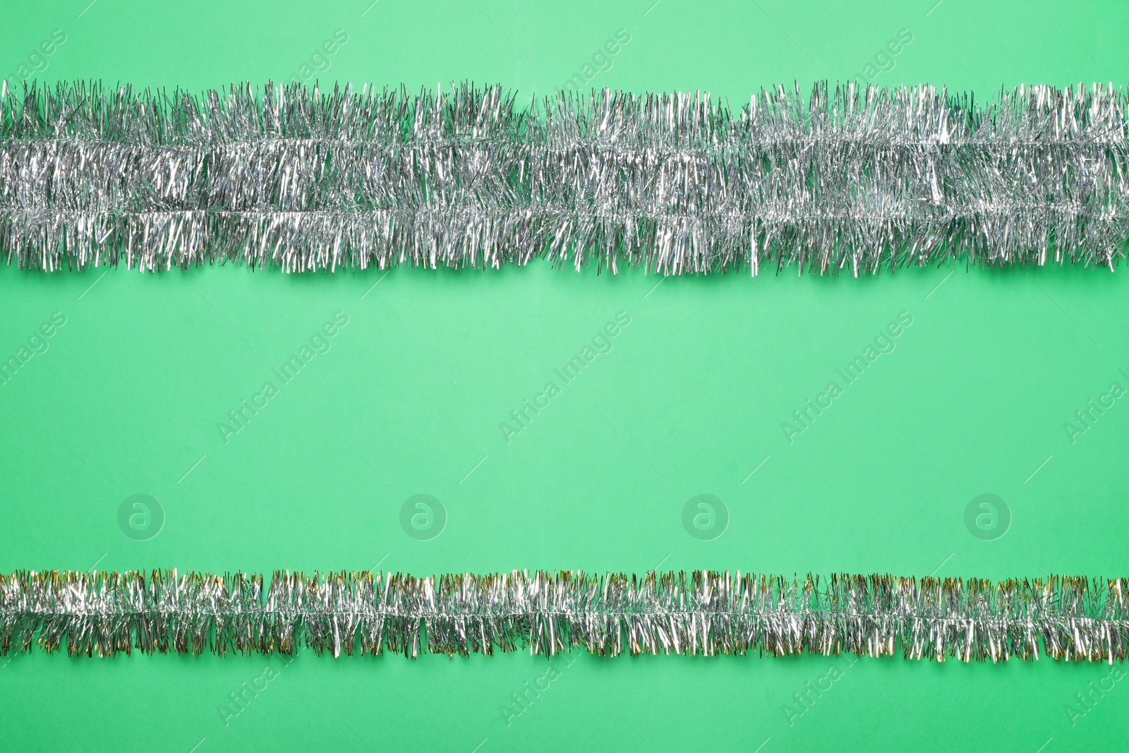 Photo of Silver tinsel on green background, flat lay. Space for text
