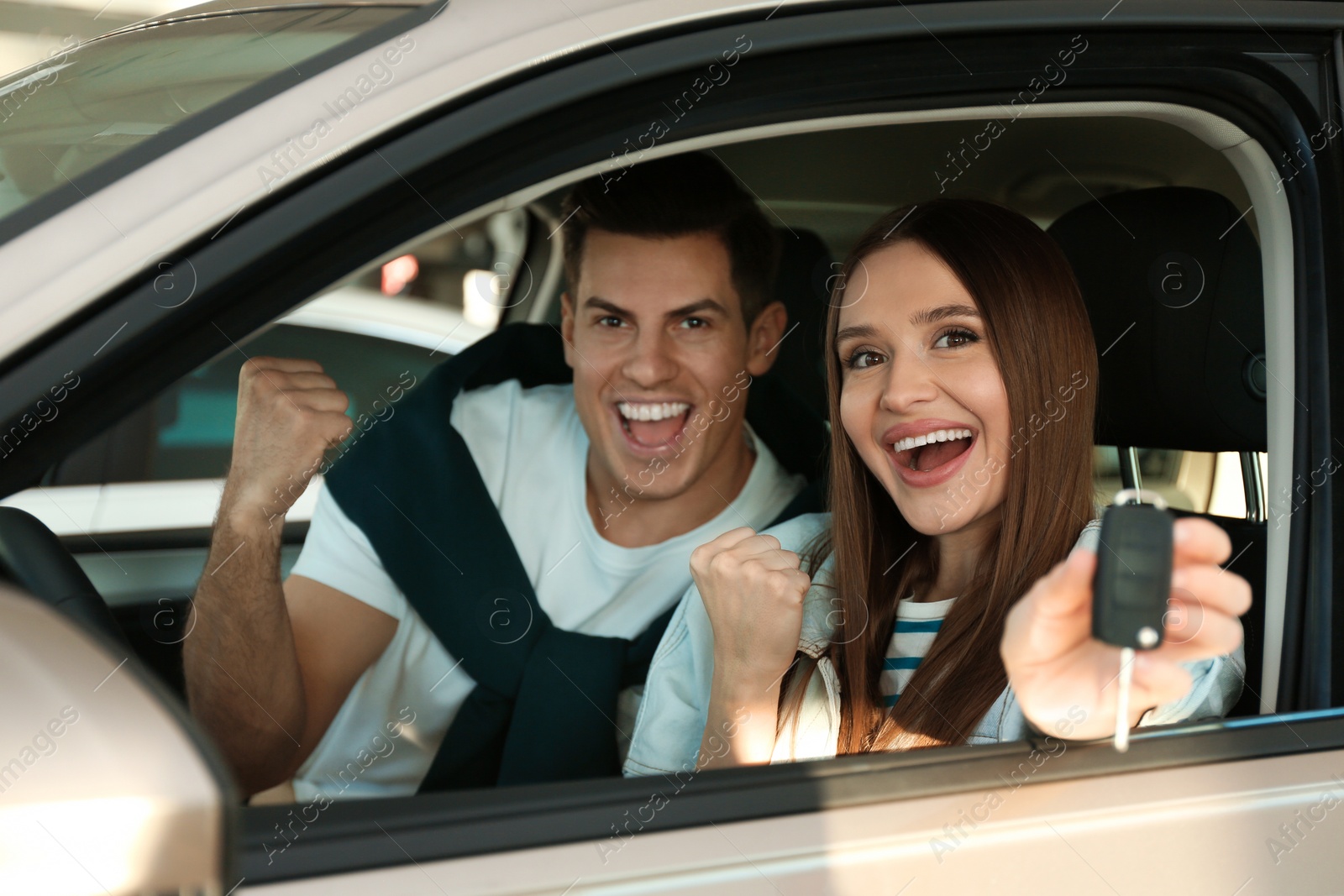 Photo of Happy couple with car key sitting in modern auto at dealership