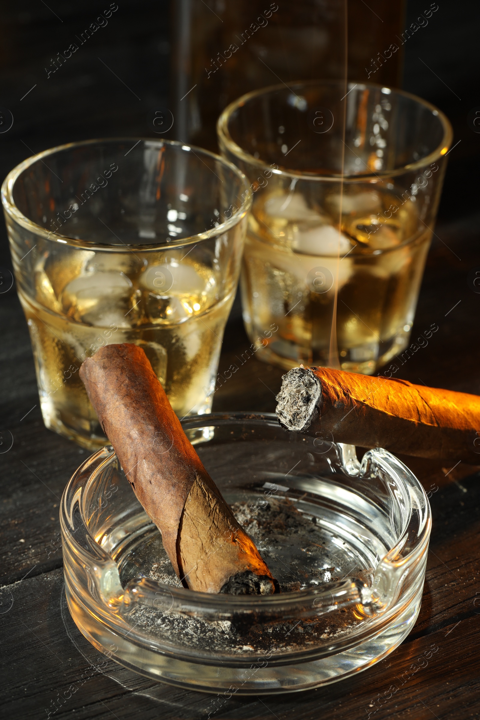 Photo of Cigars, ashtray and whiskey with ice cubes on black wooden table