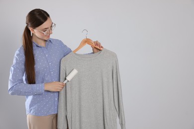 Woman cleaning clothes with lint roller on light grey background, space for text