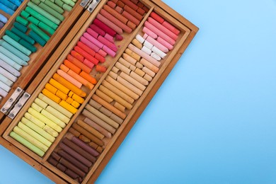 Photo of Set of soft pastels in wooden box on light blue background, top view with space for text. Drawing material
