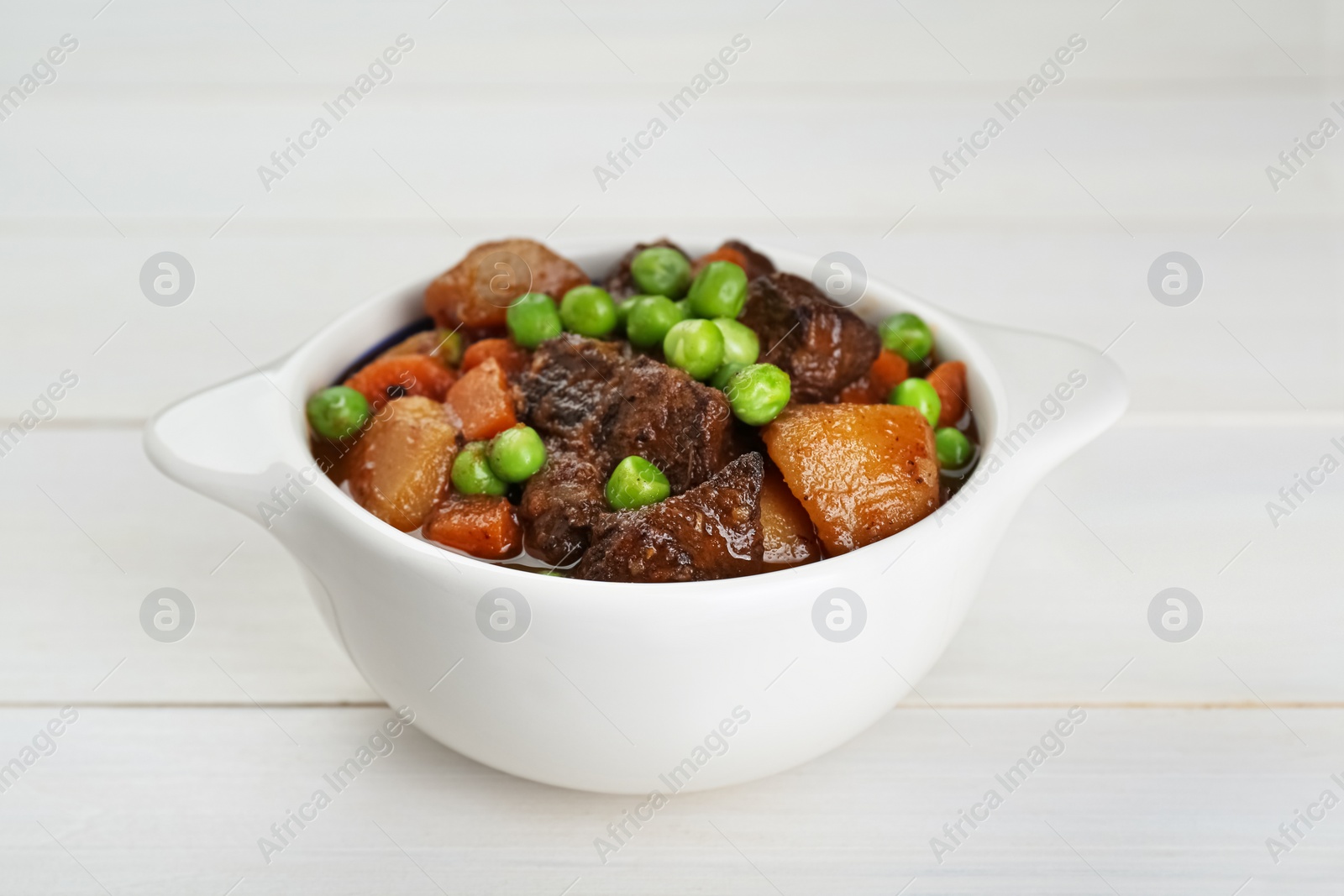 Photo of Delicious beef stew with carrots, peas and potatoes on white wooden table, closeup