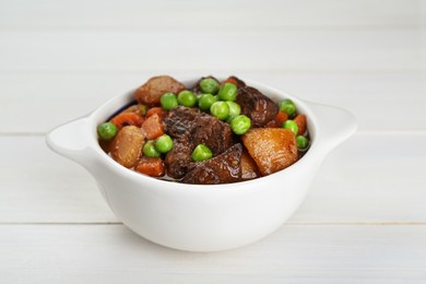 Delicious beef stew with carrots, peas and potatoes on white wooden table, closeup