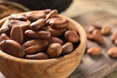Photo of Wooden bowl with cocoa beans on table, closeup